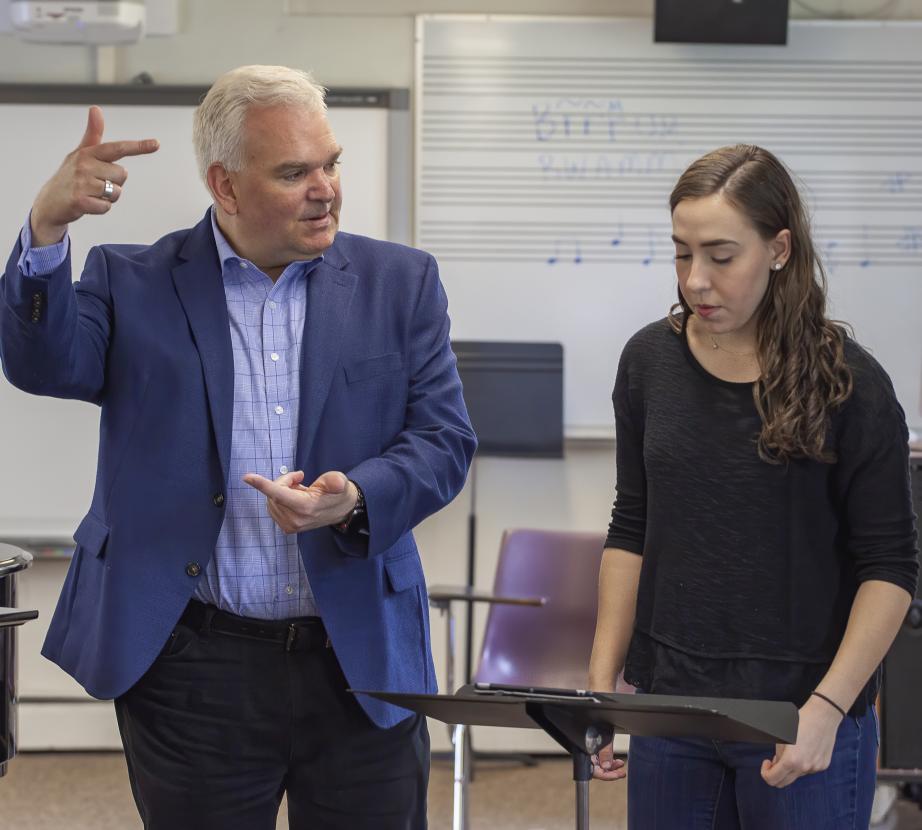 Male faculty member works with female student showing examples of conducting arm movements