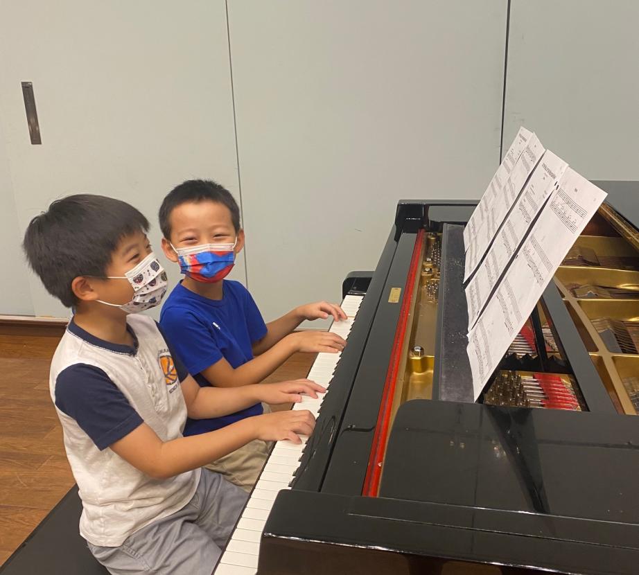 Two masked students playing piano
