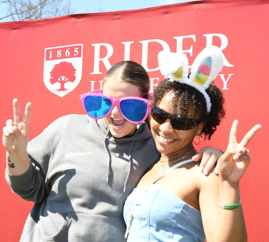 Two students pose wearing bunny years and large glasses at Rider's egg hunt