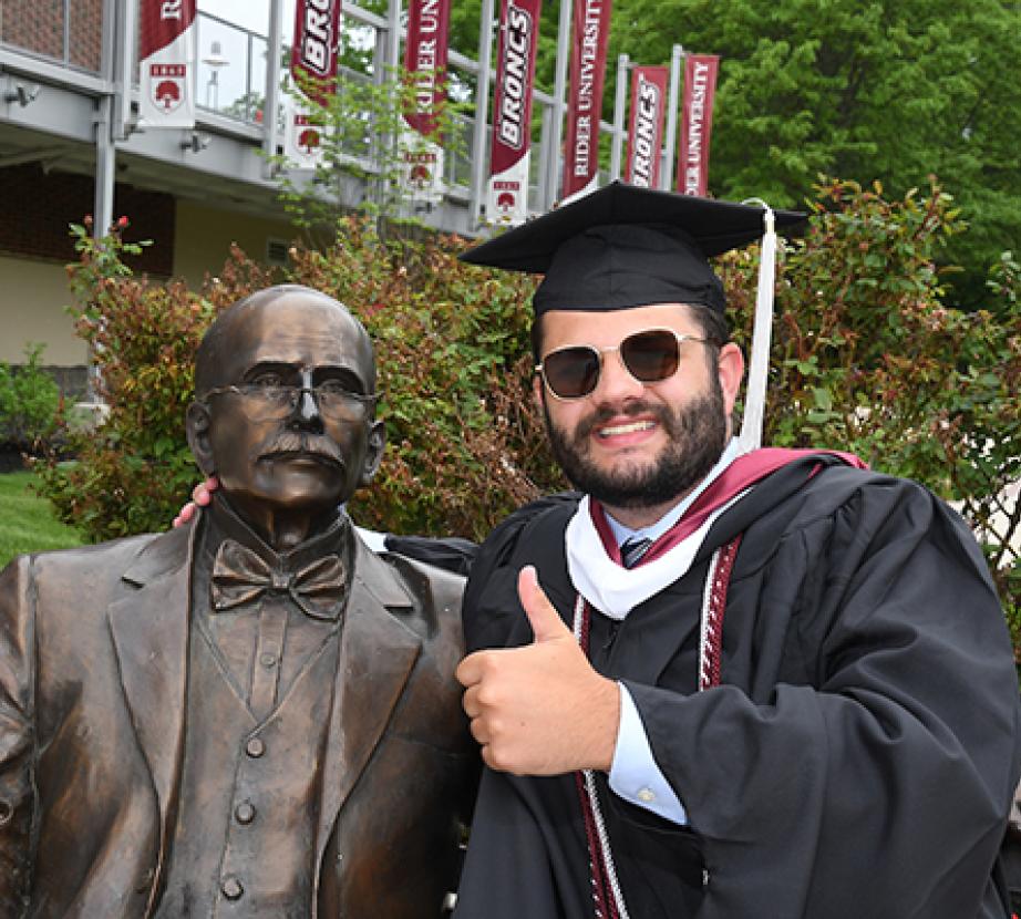 Rider graduate poses with Andrew J. statue and gives thumbs up