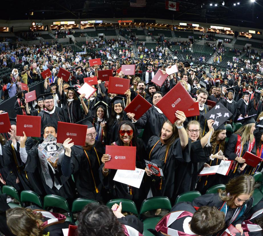 Group of graduates hold up their diplomas at Commencement