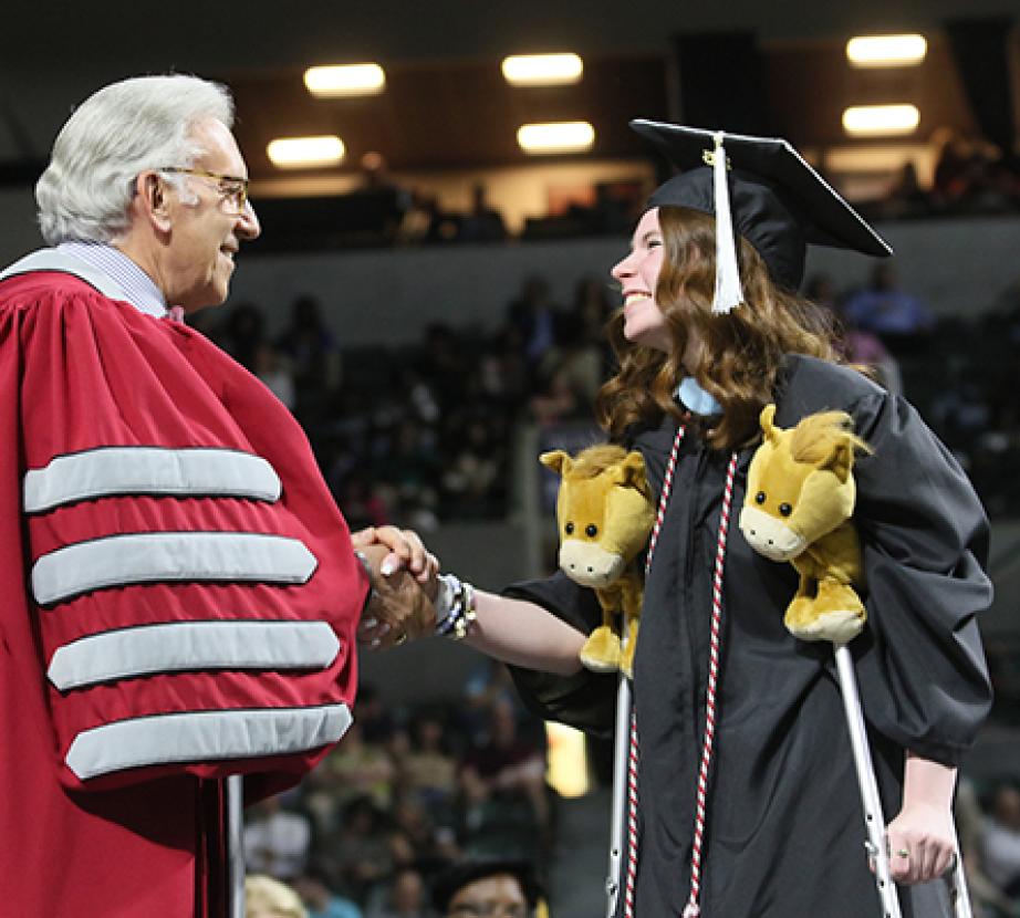 A graduate on crutches shakes hands with President Dell'Omo on the Commencement stage