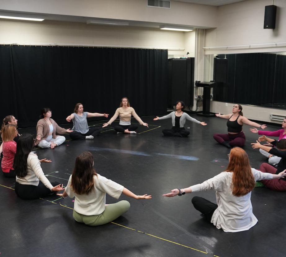 Dance/Movement Therapy students sit in a circle with arms outstretched