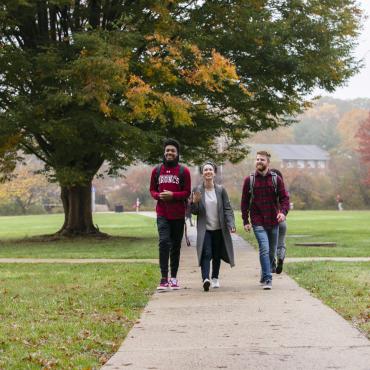 Three students walking across autumn campus