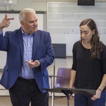 Male faculty member works with female student showing examples of conducting arm movements