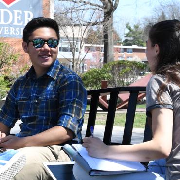 Two students sit on bench talking