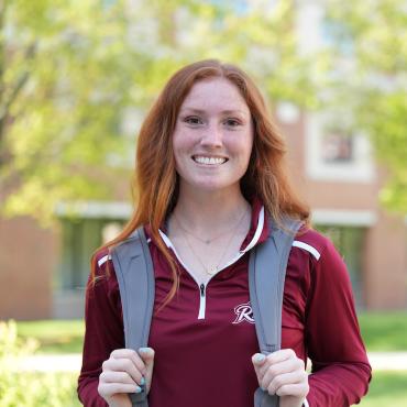 Female student with red hair and Rider logo shirt smiles at camera