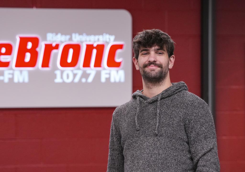 Owen McCarron stands in front of a sign for 107.7 The Bronc 